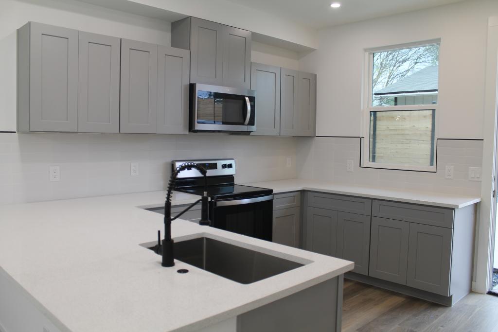 Picture of modern kitchen with medium grey cabinets and white countertops with black appliances and faucet fixtures.